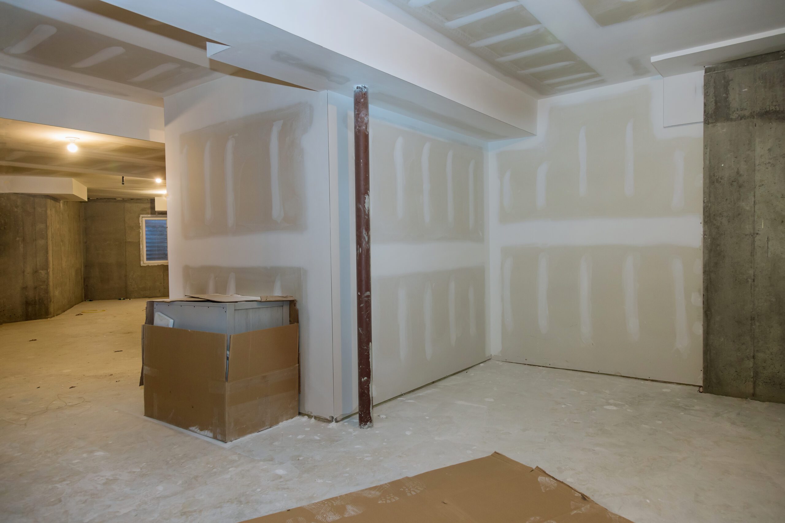 A basement in progress with drywalled walls, joint compound seams, and a concrete floor.