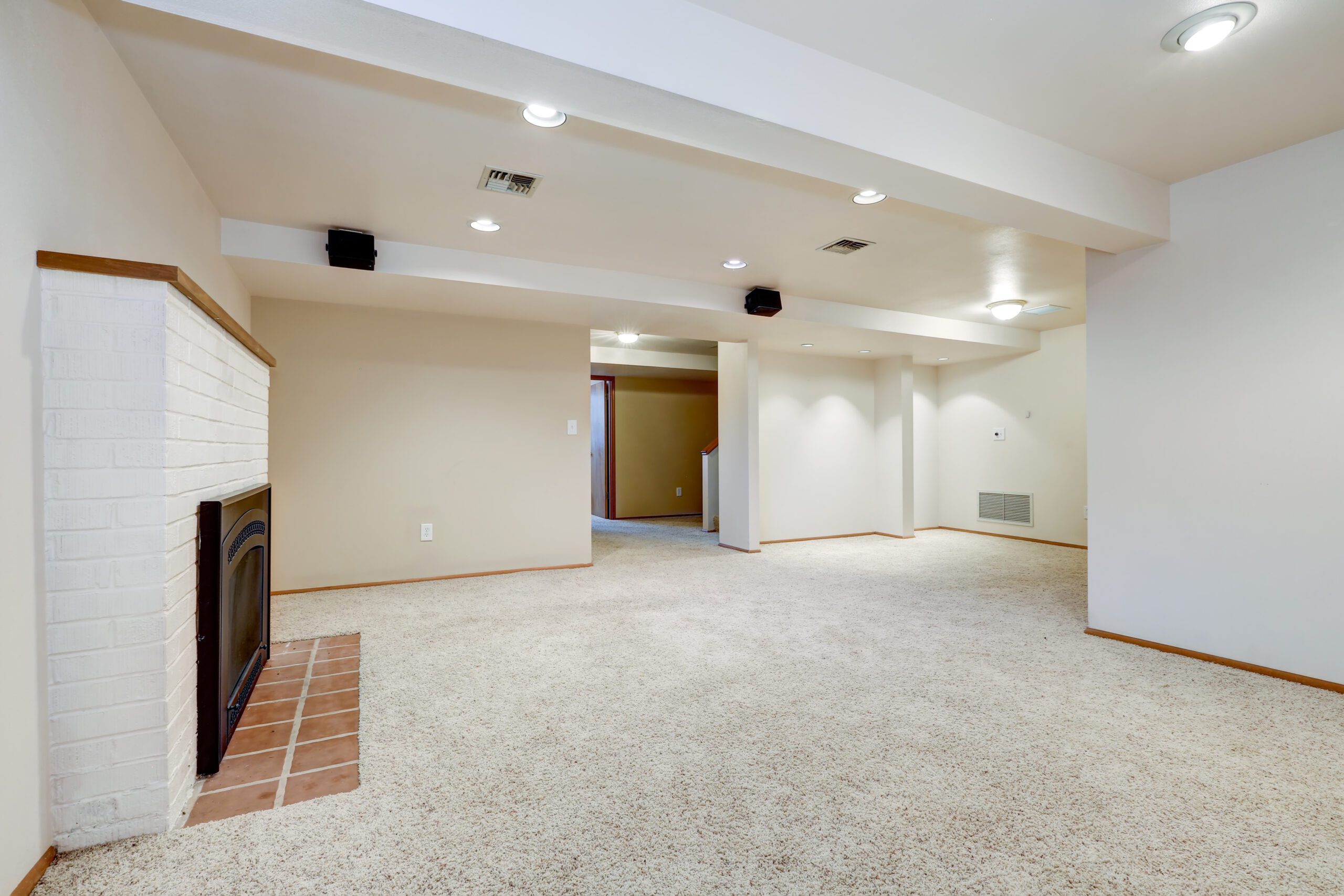 A remodeled basement with light beige walls, recessed lighting, a plush carpet, and a white fireplace.